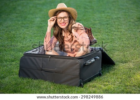 Sexy beautiful travel woman sitting in huge suitcase over green grass background. Happy travel woman plan vacation concept, copy space