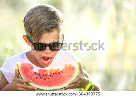 Funny kid eating watermelon outdoors in summer park, focus on face. Child, baby, healthy food