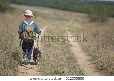 Boy with dog on a trip on the narrow rural road in sunny autumn day