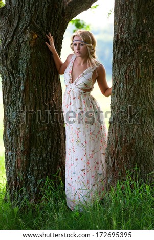 Beautiful girl in  long dress with a bright trunks of large trees