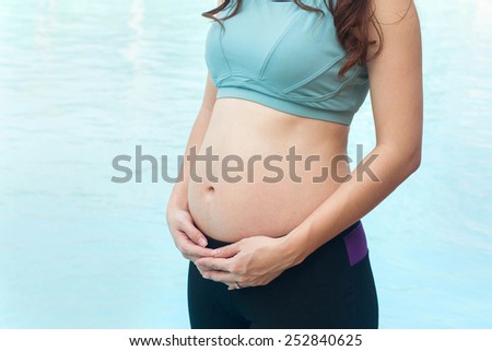 Happy beautiful pregnant woman watching her big belly in the water