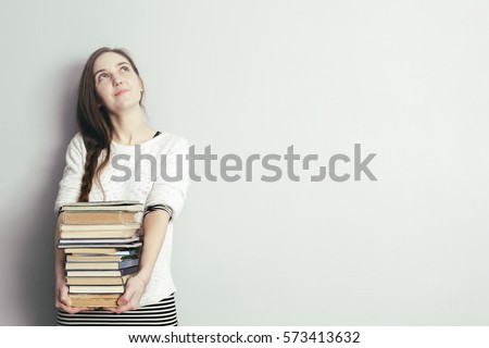 girl with long hair holding a pile of books and looking away. Get education or hobby books.