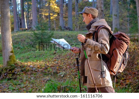 Young man traveler exploring the map in autumn forest.