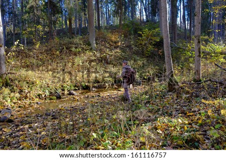 A young man walks in the forest near creek.