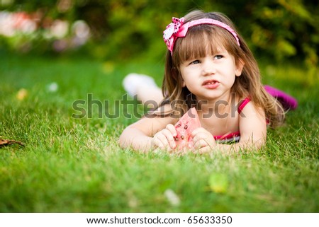 cute little girl eating water-melon on the grass in summertime