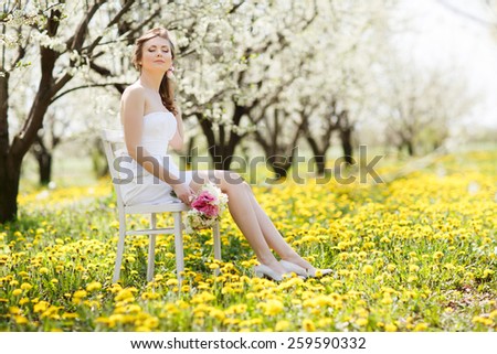 Portrait of nice dreamy girl sitting down under blooming flowers on apple tree on fresh green grass in spring garden background