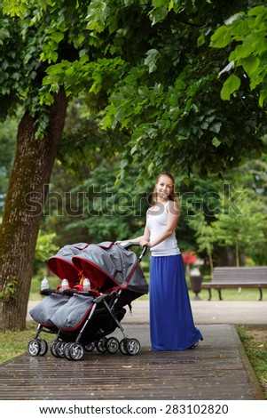 Young beautiful woman in a park with a double jogging stroller with two kids, her identical twin daughters
