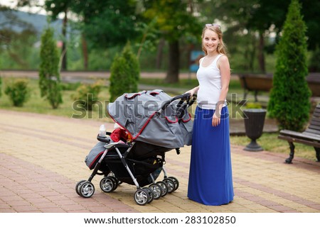 Young beautiful woman in a park with a double jogging stroller with two kids, her identical twin daughters