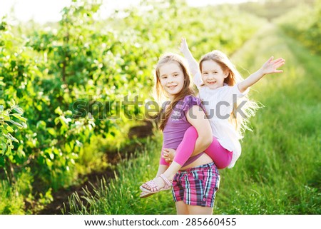 A young girl carrying  sister on her back as they play outdoor in the park