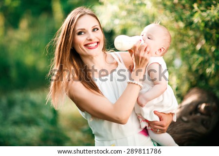 Beautiful young mother is feeding her baby from a bottle outdoor. Outdoor Portrait of happy family