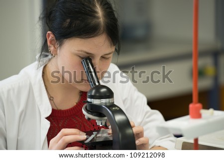 Young woman in university laboratory works with microscope
