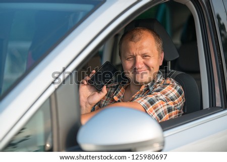 young man driving car and holding smart phone in his right hand