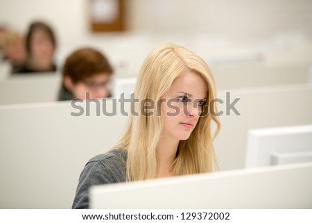 young blond girl works with desktop computer, on background other girls working