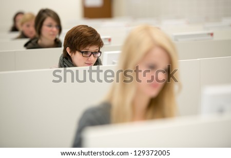 brunett girl works with desktop computer, other girls blurred work with computer too