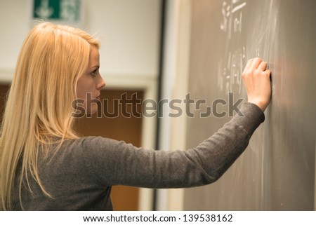 female student standing in the front of blackboard, writing mathematical formulas