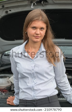 Young business woman standing in front of a car. Car hood is open.