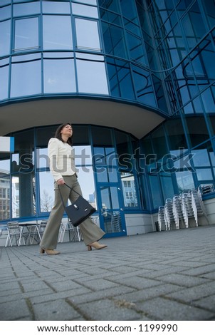 business woman with bag and mobile phone walking in front of skyscraper