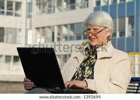 mature woman works with laptop sitting on bech in front of office building