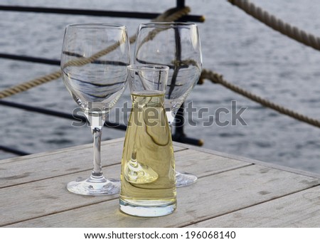 Two empty glasses and bottle of white wine on the wooden table with sea at the background