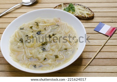 A plate of french onion soup with a small french flag and a slice of bread with melted cheese