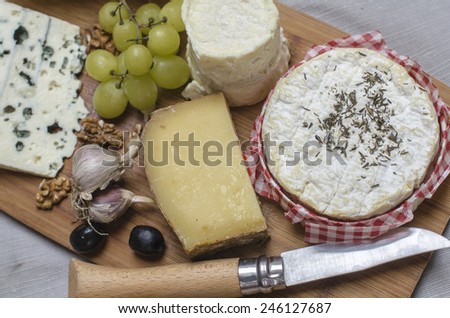 A wooden desk with various french cheese, grapes, olives and a knife
