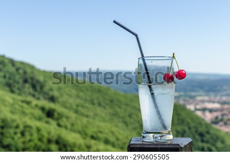 A glass of lemonade with a cherry and mountain background in a cafe