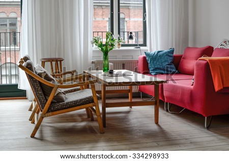 A beautiful living room with red sofa, wooden tables and flowers