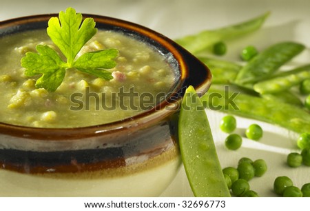 A bowl of Pea Soup with peas and pea pods surrounding it.
