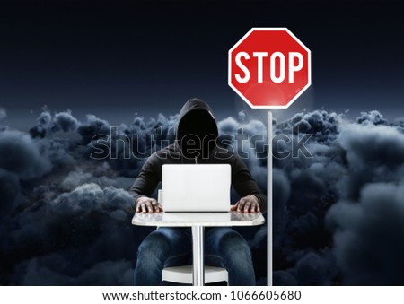 Hacker working on laptop close to a stop board in front of cloudy background