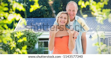 Happy older couple holding paint roller against pretty house with a blue and white filter