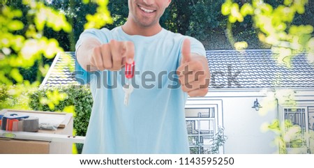 Man holding out new house key while gesturing thumbs up against pretty house with a blue and white filter