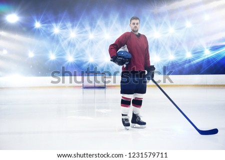 Portrait of ice hockey player holding helmet and stick against view of strong blue lights
