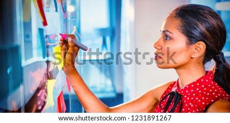Female executive writing on glass board with a marker in office