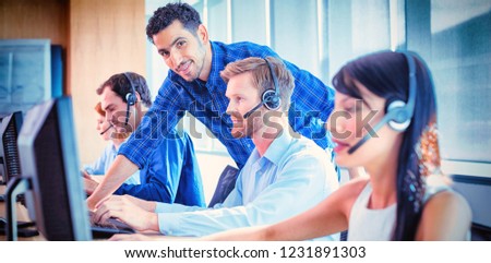 Smiling male supervisor assisting telemarketer at desk in call center
