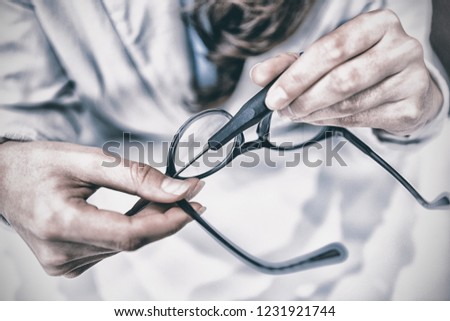 Mid section of optician repairing spectacles with tool in optical store