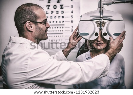 Smiling optometrist examining female patient on phoropter in ophthalmology clinic