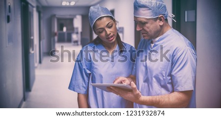 Surgeons discussing over digital tablet in hospital corridor