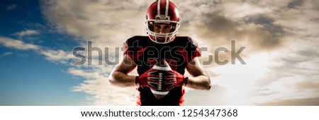 American football player standing with helmet and ball against cloudy sky over countryside