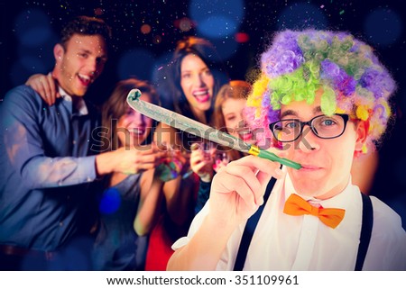 Geeky hipster wearing a rainbow wig blowing party horn against happy friends drinking shots smiling at camera