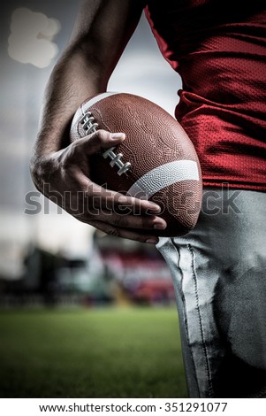Cropped image of sportsman holding American football against pitch