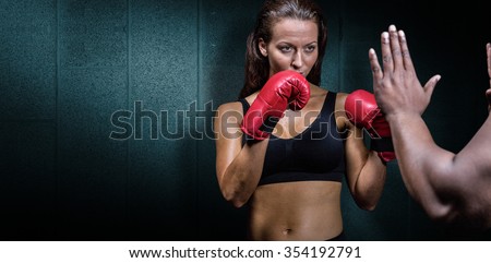 Female boxer with fighting stance against trainer hand against dark grey room