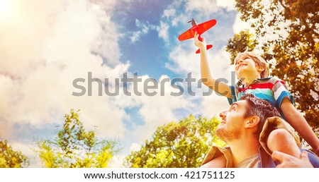 Low angle view of a boy with toy aeroplane sitting on fathers shoulders at the park
