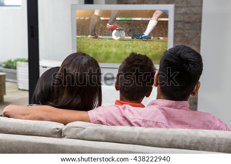 Happy family watching tv on the sofa against football players tacakling for the ball on pitch