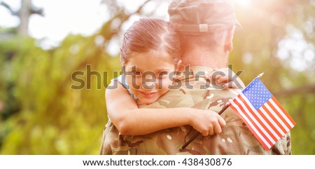 Portrait of smiling girl holding american flag while hugging army officer father in park