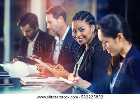 Portrait of businesswoman using digital tablet while colleagues writing notes in office