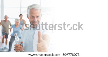 Man showing thumbs up sign with people exercising in background at fitness studio