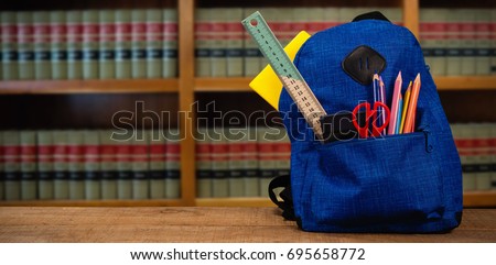 Schoolbag on wooden table against volumes of books on bookshelf in library