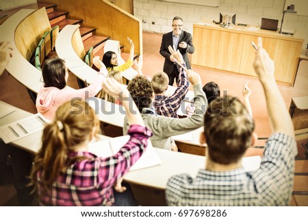 Rear view of students raising hands with teacher in college lecture hall