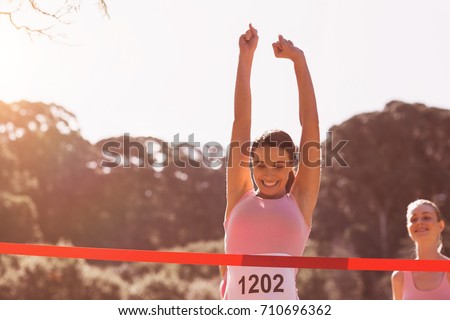 Happy female athlete with arms raised crossing finish line on sunny dy