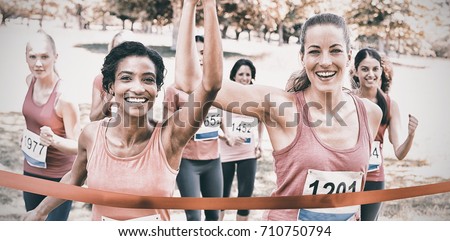 Portrait of happy female breast cancer participants crossing finish line at marathon race in park